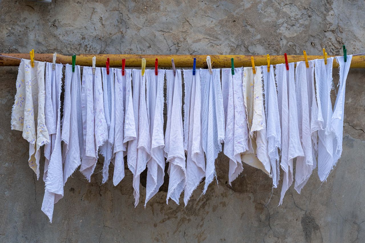 Home Neatly arranged white fabrics drying under the sun, held by colorful clothespins against a rustic wall.