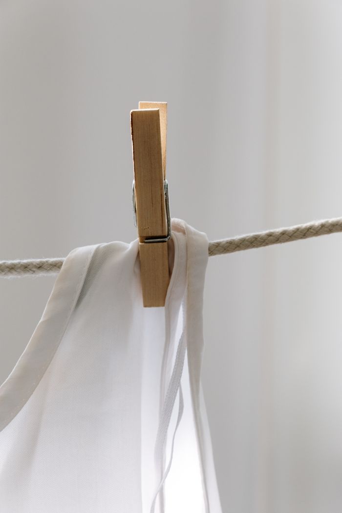 Minimalist photo of a wooden clothespin holding a white fabric on a rope, indoors.